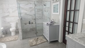 Baño con ducha envuelta en vidrio, inodoro, tocador con lavamanos y puerta con ventana.