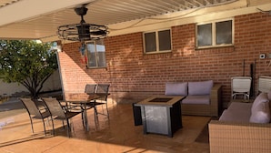 Un espace extérieur aménagé en patio, avec un mur en briques, un ventilateur de plafond, une table avec des chaises et un canapé.