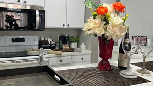 Uma cozinha moderna com armários brancos, micro-ondas, espaço para café e um vaso com flores.