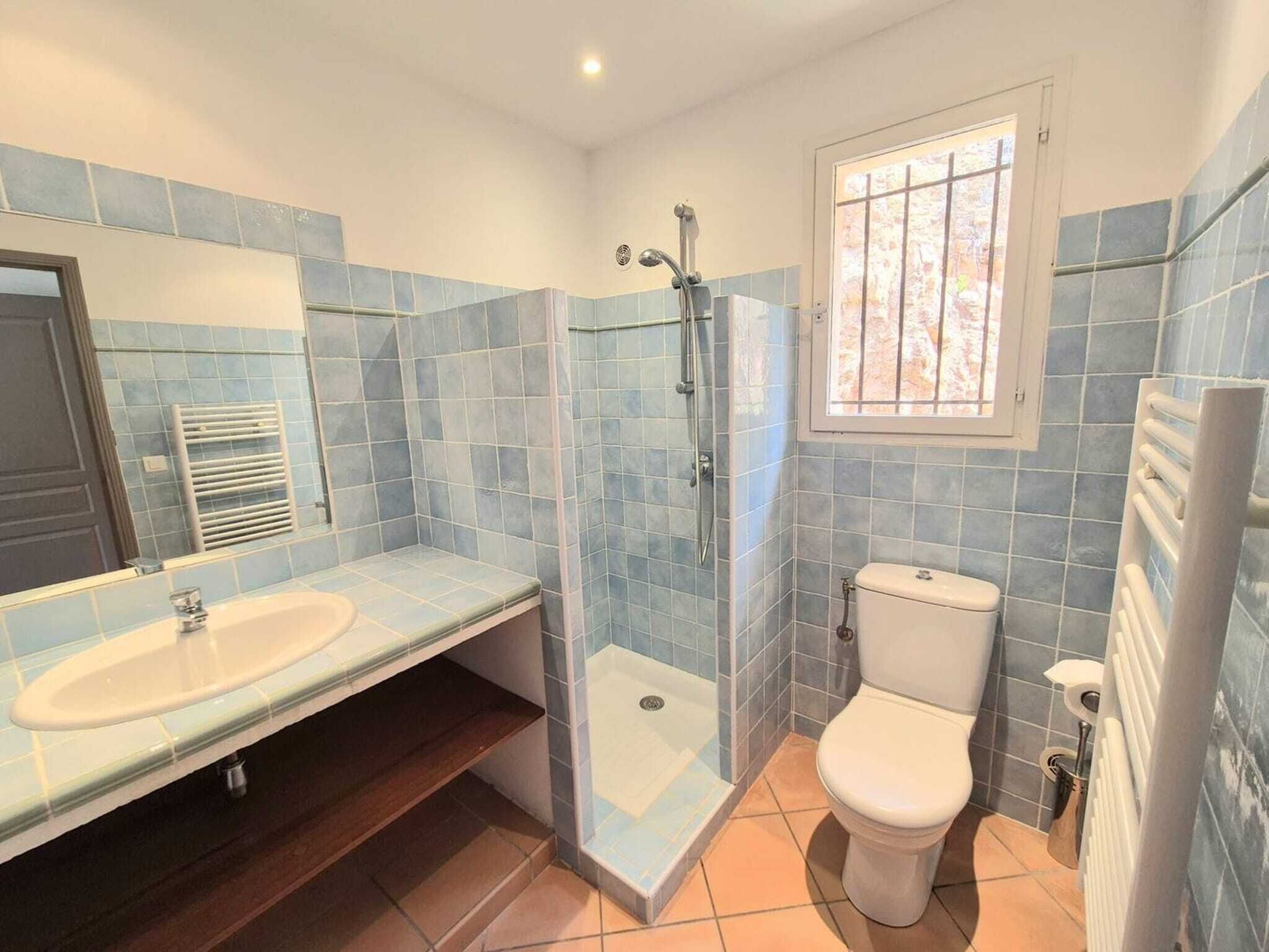Un baño con ducha, inodoro y lavamanos, con azulejos azules y una ventana.