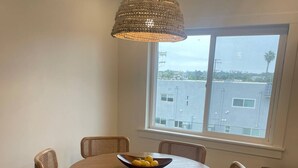 Een eetgedeelte met een ronde houten tafel, zes rieten stoelen en een geweven hanglamp.