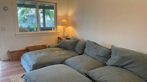 Een moderne woonkamer met een modulaire bank, een bijzettafeltje met een lamp, rieten manden en een raam met uitzicht op groen.