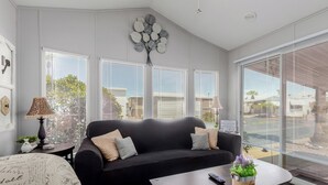 A living room with a black sofa, a coffee table with a plant, and large windows with blinds. - Updated 1-bedroom queen/ Free WiFi, AC Resort of Greenfield Village Mesa 55+ (Mesa)