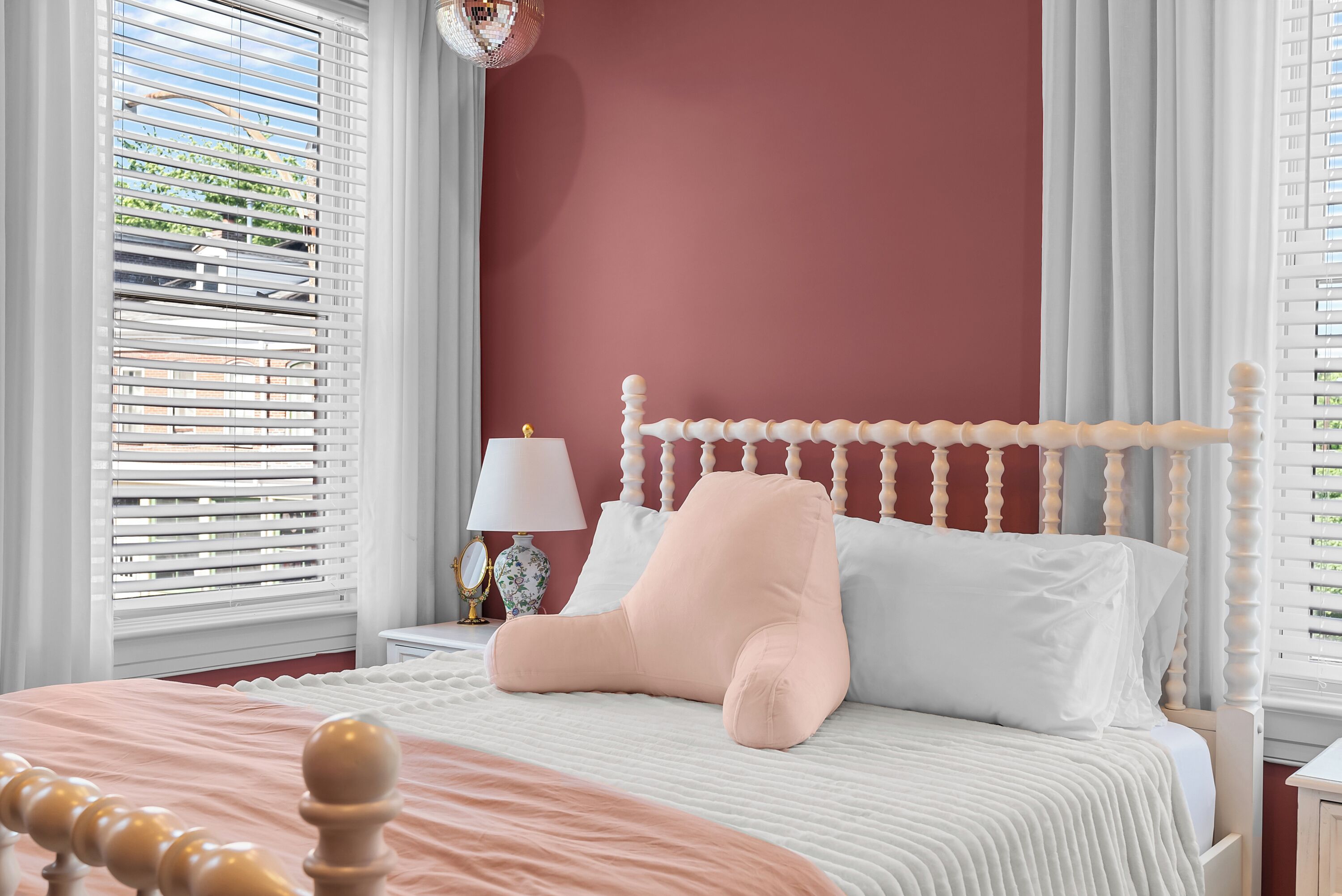 Une chambre à coucher avec un cadre de lit en bois, une literie blanche et un coussin décoratif rose.