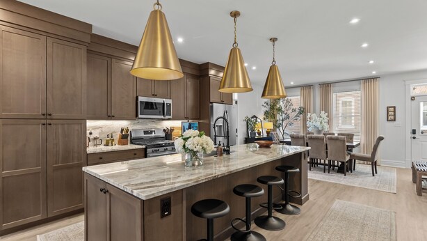 A modern kitchen with wooden cabinets, a marble island with bar stools, pendant lighting, and a dining area with a table and chairs.
