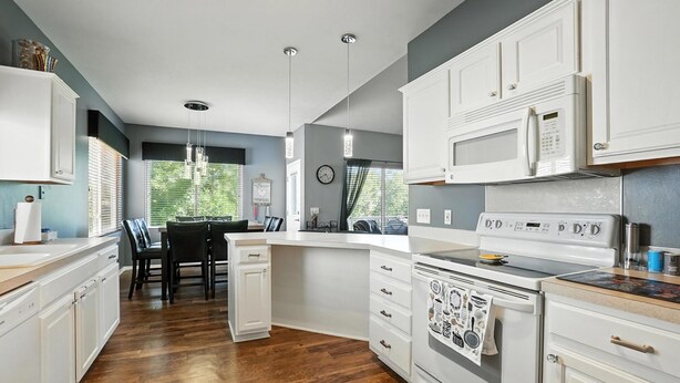 Une cuisine moderne avec des meubles blancs, un plancher en bois et un coin repas comprenant une table et des chaises.