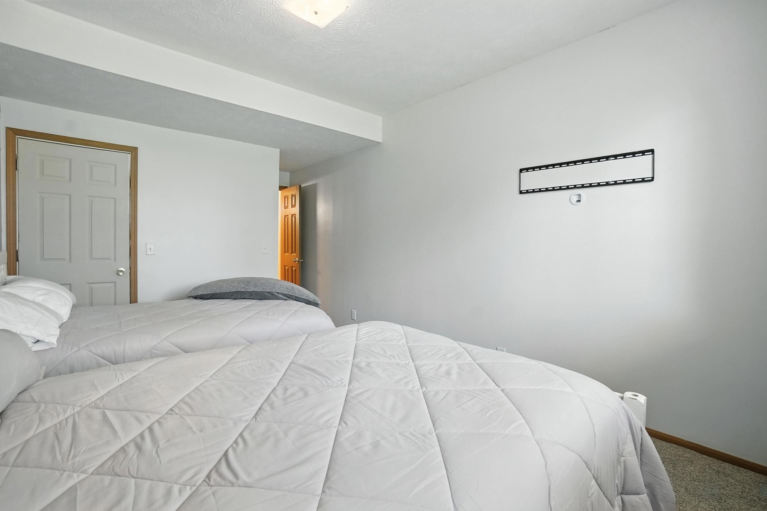 A bedroom with two beds, a door, and a light switch on the wall.