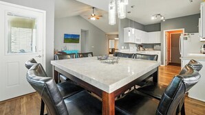Une cuisine moderne avec des meubles blancs, un coin repas doté d’une table en marbre et un ventilateur de plafond.