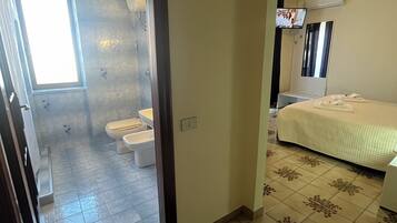 Une chambre d’hôtel équipée d’une douche, de toilettes, d’un lit et d’un téléviseur fixé au mur.