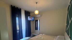 A hotel room with a bed, a bedside table with a lamp, a TV on the wall, and a window with curtains.