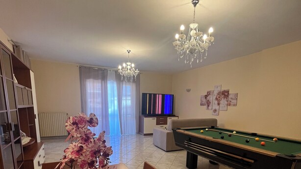 A living room with a pool table, a dining table with chairs, a chandelier, and a television.
