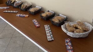 A breakfast buffet with labeled baskets of bread and pastries, a wall sign saying "OK, but first Coffee!", and a framed "Breakfast" sign.