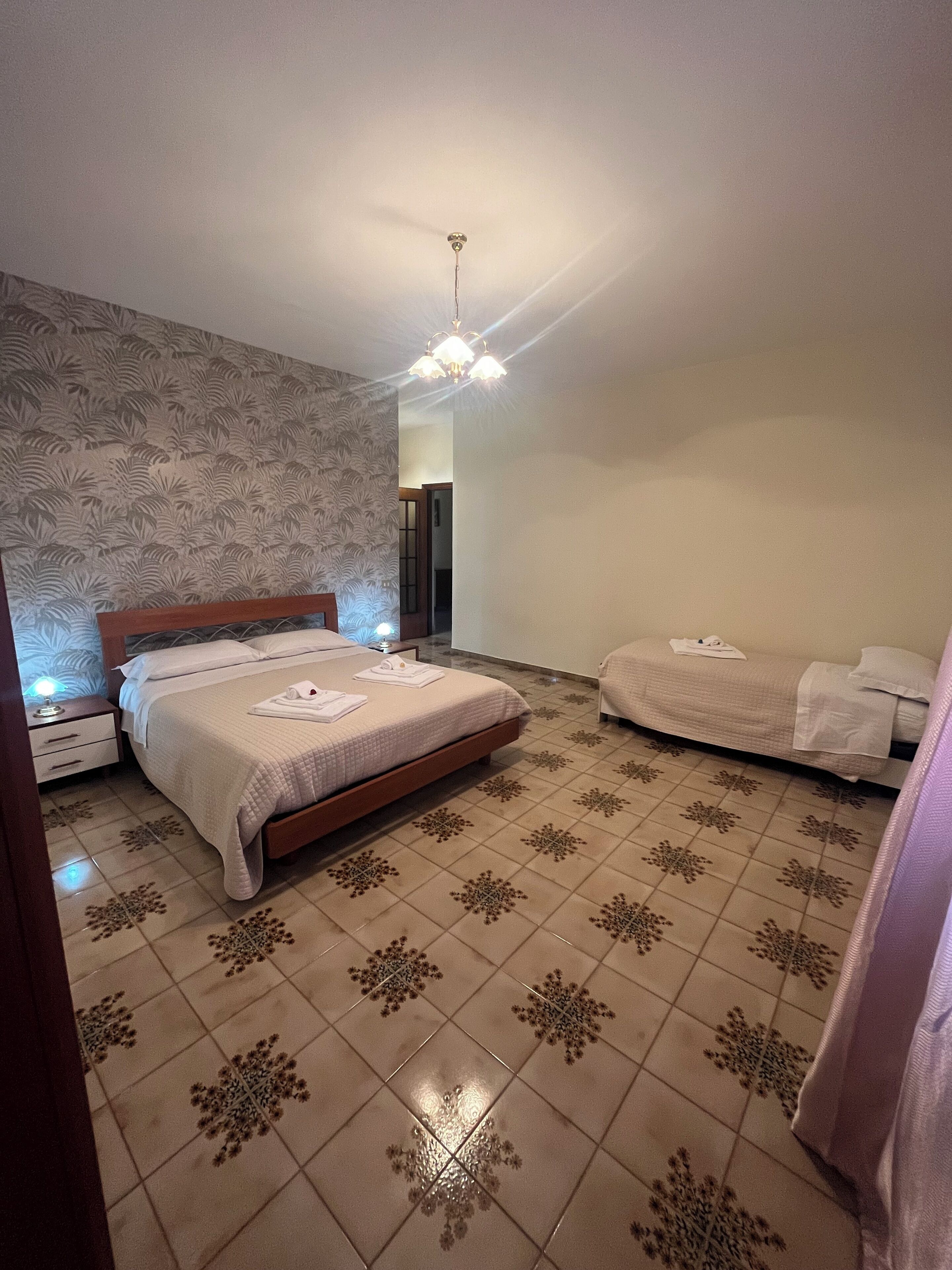 Ein Schlafzimmer mit Bett, Nachttischen, einer Wand mit Muster und einer Deckenleuchte.