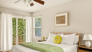 A bedroom with a bed, a nightstand, a lamp, a ceiling fan, and a window with curtains. - Serene SoCo Escape — Walk to Cafes + Free Parking/In-Unit Laundry! (Austin)