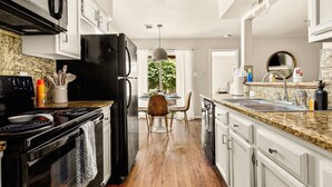 A modern kitchen with granite countertops, a black refrigerator, and white cabinetry. - Serene SoCo Escape — Walk to Cafes + Free Parking/In-Unit Laundry! (Austin)