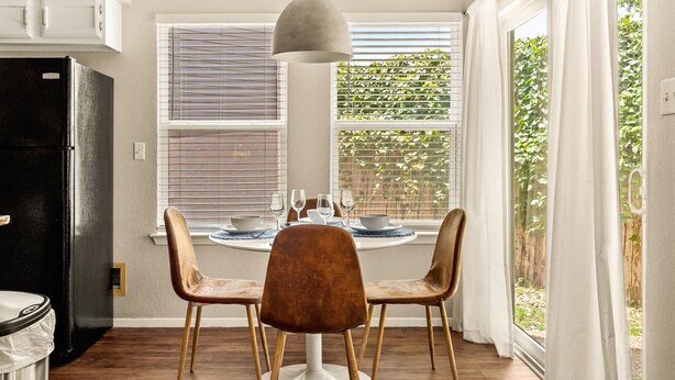 A dining area with a round table, two chairs, a pendant light, and a window with blinds. - Serene SoCo Escape — Walk to Cafes + Free Parking/In-Unit Laundry! (Austin)
