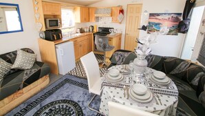 Un espace de vie compact comprenant un coin cuisine, un coin repas avec une table pour quatre personnes et un canapé agrémenté de coussins à motifs.