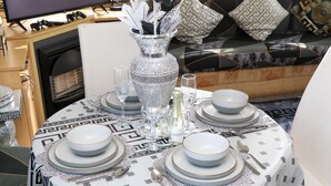 Une table de salle à manger ronde, mise avec des assiettes, des bols, des verres et des couverts, et entourée d’une nappe à motifs.