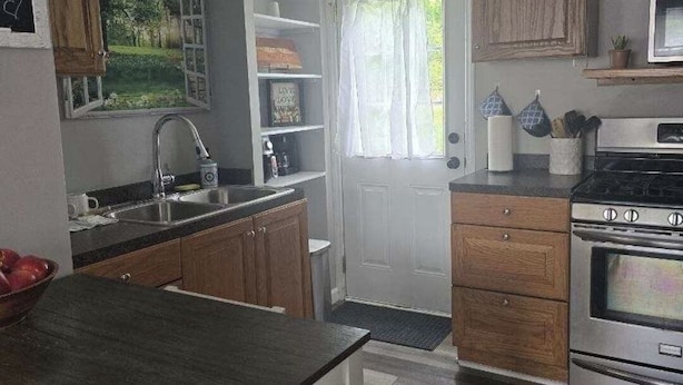 A compact kitchen with wooden cabinets, a built-in oven, and a window with curtains.