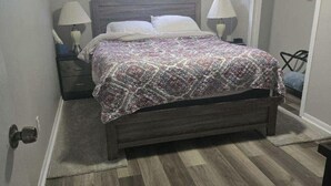 A bedroom with a wooden bed, two bedside tables with lamps, a window with curtains, and a wardrobe with a hanging rod.