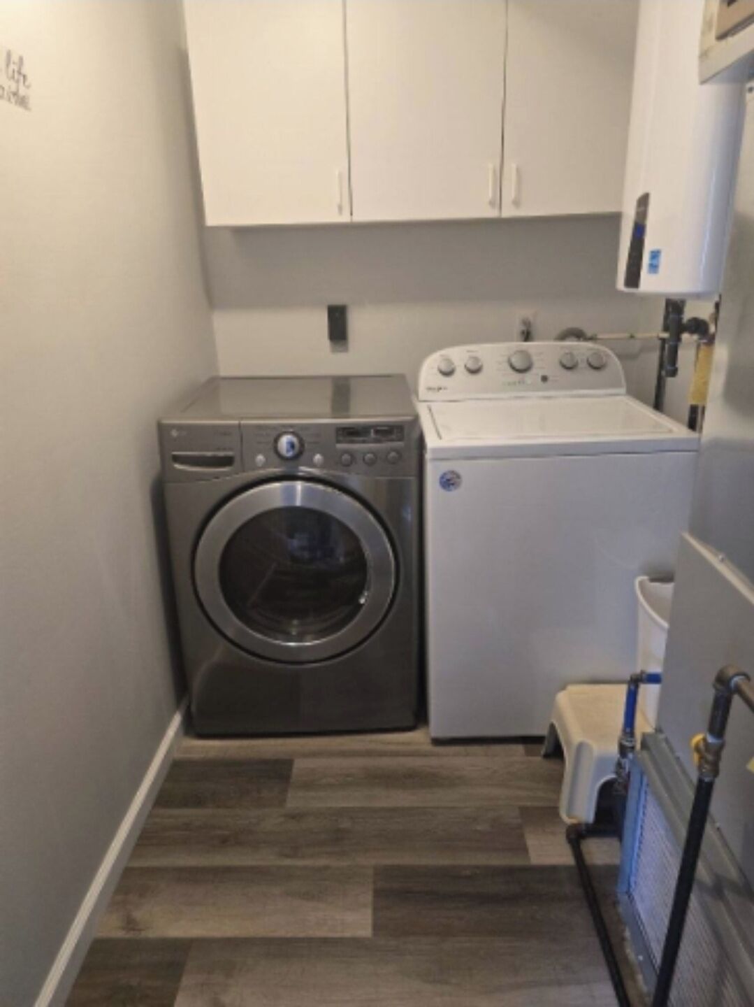 A compact laundry room with a front-loading washer and dryer, wooden flooring, and white cabinets.