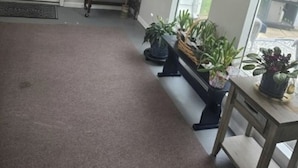 A hallway with a white door, a welcome sign, a bench, and potted plants.
