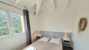 A bedroom with a bed, two bedside tables with lamps, a window with curtains, and a view of greenery outside. - F2 - Casina n° 5 - 1 Bedroom - Sea View (PORTO VECCHIO)