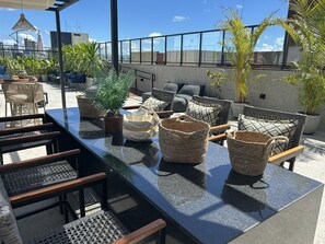 Une terrasse sur le toit, aménagée avec du mobilier d’extérieur, des plantes en pot et offrant une vue dégagée sur le panorama urbain.