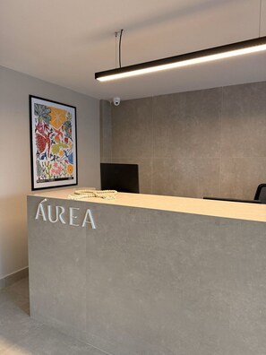 Un comptoir d’accueil avec une enseigne indiquant « AUREA », une œuvre d’art encadrée accrochée au mur et une caméra de surveillance placée au-dessus du comptoir.