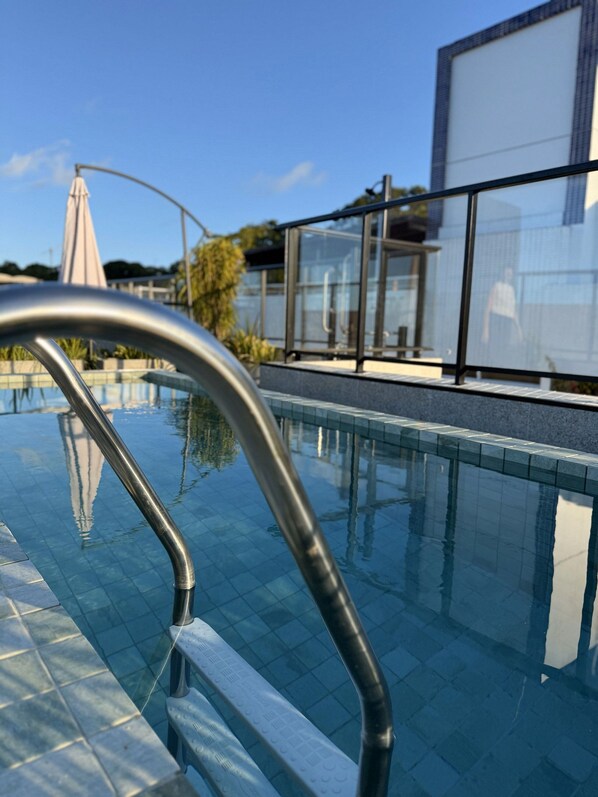 Une piscine moderne avec une eau d’un bleu limpide, des garde-corps en métal et une structure en verre en arrière-plan.