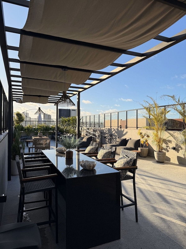 A rooftop terrace with outdoor seating, a table, and potted plants.