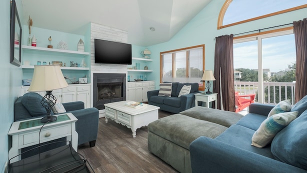 A living room with a fireplace, a television, and a large window with curtains.