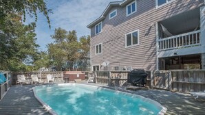 A backyard with a swimming pool, deck chairs, and a wooden fence.