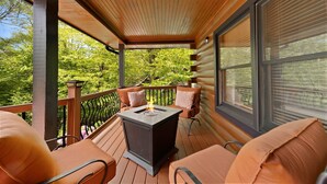 A covered deck with a fire pit, wooden railing, and cushioned seating.