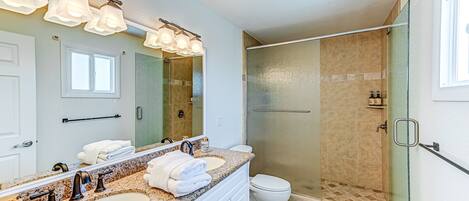 A modern bathroom with a double sink vanity, a large mirror, a glass-enclosed shower, and a toilet.