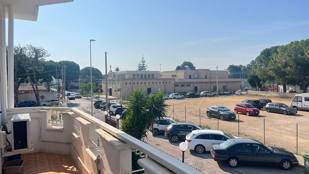 A parking area with multiple cars, a building with a flat roof and cross-shaped windows, and a clear sky. - Superior Two-room Apartment – ALH Hotel Digitale (Taranto)