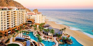 Ein Resort mit mehreren Swimmingpools, einem Strand und einer Bergkulisse.