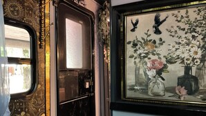 Una habitación con cama, ventana con vistas, un cuadro de flores y una puerta con diseño decorativo.