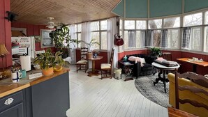 A cozy room with a wooden ceiling, a dining area with chairs and a table, a sofa, and a window with curtains. - Cozy Bed & Breakfast in Magical Eureka Springs with WiFi, AC -Sunset View Room (Eureka Springs)