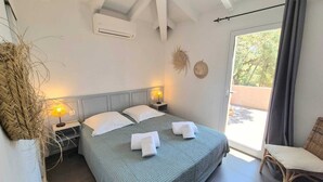 A bedroom with a bed, two bedside tables with lamps, a window with curtains, and a view of the outdoors.