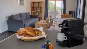 A cozy living area with a sofa, a coffee machine, a basket of croissants, and a coffee cup.