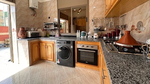 A modern kitchen with a built-in washing machine, a stove, and a large island with various appliances and cookware. - Charming 4-bedroom villa in enchanting مراكش with WiFi, AC.pool (مراكش)