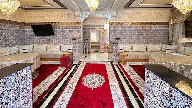 A luxurious room with ornate tile walls, a red and white patterned carpet, and two sofas with a small table in between. - Charming 4-bedroom villa in enchanting مراكش with WiFi, AC.pool (مراكش)