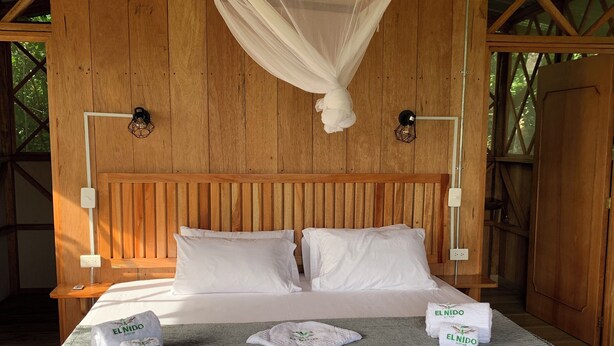 A wooden-framed room with a bed, white bedding, and a mosquito net.