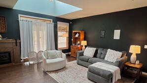 A living room with a skylight, two sofas, a white armchair, a wooden cabinet, and a patterned rug. - Private Oasis Close to the City (LaFayette)