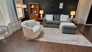 A living room with a dark blue wall, a grey sofa, a white armchair, and a patterned rug. - Private Oasis Close to the City (LaFayette)