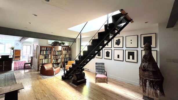 Un salon spacieux doté d’un parquet en bois, d’un escalier noir, d’une bibliothèque et d’une sculpture murale.