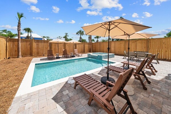A backyard with a swimming pool, lounge chairs, and umbrellas.