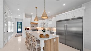 Una cocina moderna con armarios blancos, un refrigerador de acero inoxidable grande y una isla central con sillas de madera.