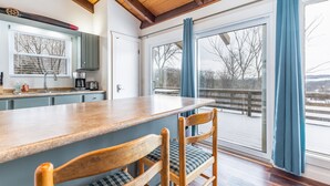 Een keuken met een houten aanrecht, twee stoelen, een raam met gordijnen en uitzicht op een besneeuwd landschap.